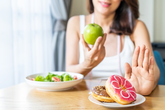 アジアの若い女性は健康的なサラダや果物を健康的に食べることを選ぶ一方で、ジャンクフードを拒否します。