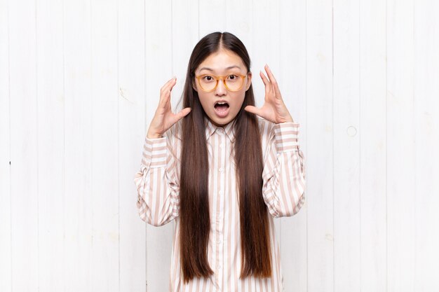 Asian young woman screaming with hands up in the air, feeling furious, frustrated, stressed and upset