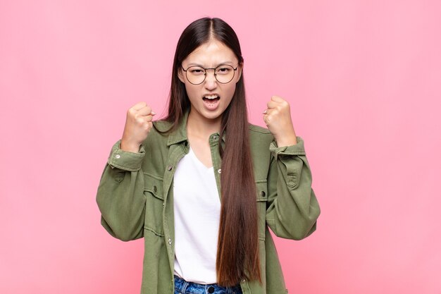 Asian young woman shouting aggressively with an angry expression