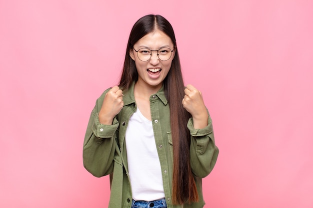 Asian young woman shouting triumphantly, laughing and feeling happy and excited while celebrating success