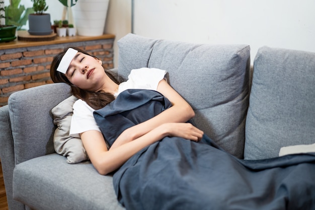 Азиатская молодая женщина больна коронавирусом или covid-19, имеющих высокую температуру, лежа на диване у себя дома.