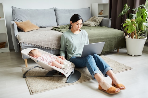 Asian young woman sitting on the floor in the room working online on laptop and caring about her lit...