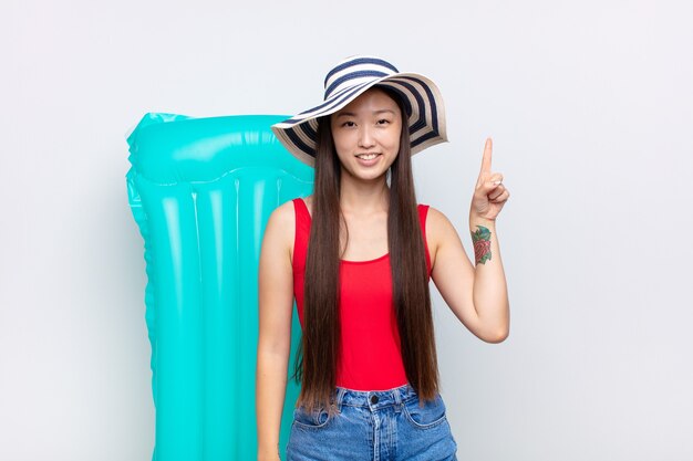 Asian young woman smiling cheerfully and happily, pointing upwards with one hand to copy space. summer concept