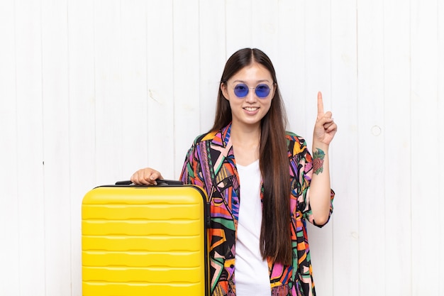 Asian young woman smiling cheerfully and happily, pointing upwards with one hand to copy space