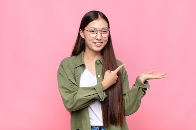 Asian young woman smiling, feeling happy, carefree and satisfied, pointing to concept or idea on copy space on the side