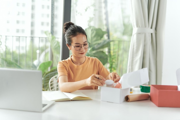 Asian young woman smiling while arranging packages with beauty products to sell at her online shop