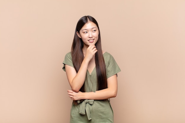 Asian young woman smiling with a happy, confident expression with hand on chin