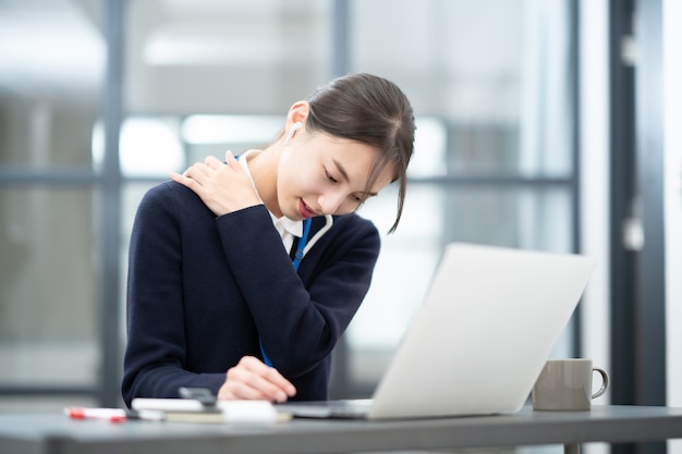 Asian young woman suffering from stiff shoulders at desk work