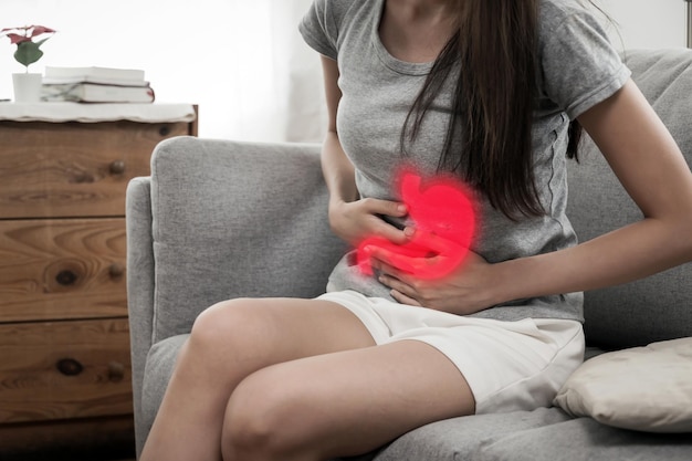 Photo asian young woman suffering stomach ache sitting on couch in living room at home medicine healthcare people painful stomachache gynecology menstrual pain medical and health care concept