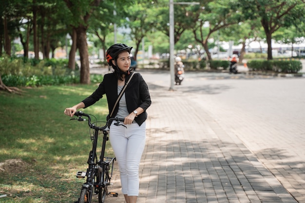 Шлем азиатской молодой женщины нося после работы гуляя с ее велосипедом