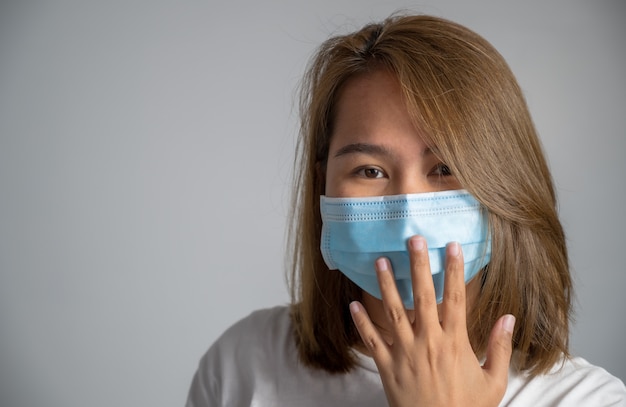 Giovane donna asiatica che indossa una maschera protettiva igienica sul viso su sfondo bianco,