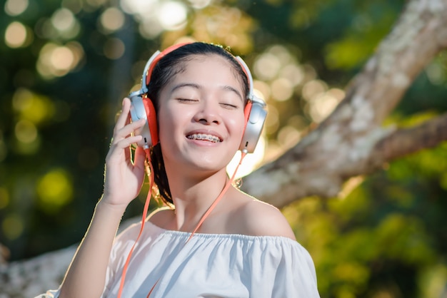 写真 ヘッドフォンと公園で夕日に音楽を聴くとアジアの若い女性。