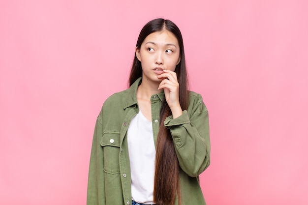 Asian young woman with surprised, nervous, worried or frightened look, looking to the side towards copy space