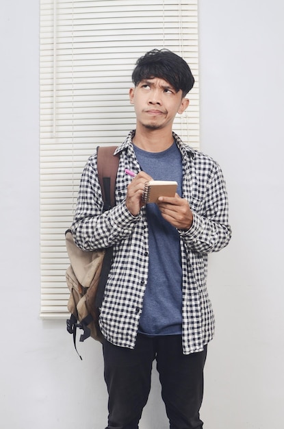 Asian youth student wearing shirt holding book while thinking and carrying backpack Education concept