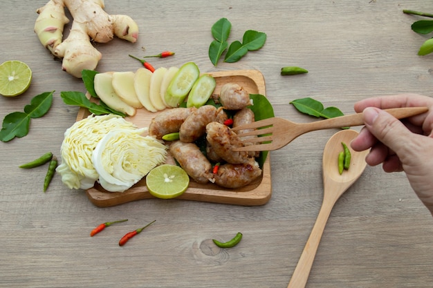 자연광으로 식사 또는 간식을 위한 아시아 맛있는 전채, 돼지고기 가공 식품, 바나나 잎으로 만든 천연 발효 신 돼지고기 랩은 야채, 칠리, 생강 베르가못, 레몬으로 장식되어 있습니다.