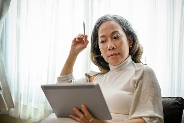 디지털 태블릿을 사용하여 집에서 원격으로 일하는 아시아계 여성 기업가