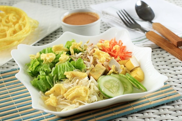 Betawi asiatico. verdure crude indonesiane e tofu giallo con salsa piccante alle arachidi di betawi, jakarta. condita con cracker gialli. servito su piatto in ceramica bianca