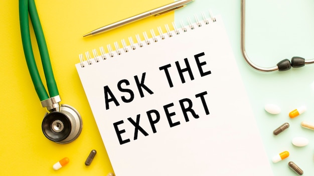 Ask the expert is written in a notebook on a color table next to pills and a stethoscope