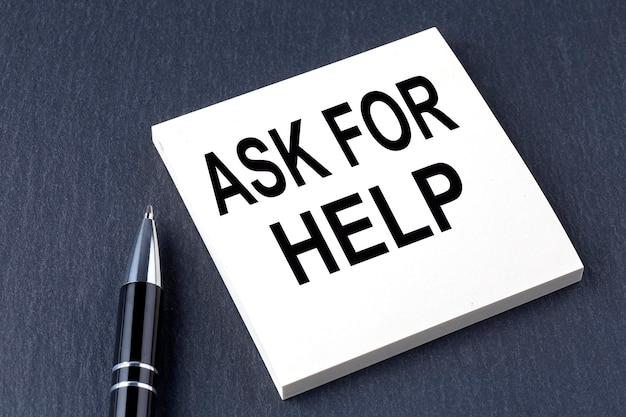 Текст ASK FOR HELP на наклейке с ручкой на черном фоне