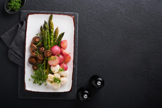 Asparagus mushrooms mozzarella cheese grilled radish and cress\
salad oil olive salad on rectangular ceramic plate on black\
concrete table background healthy diet grilled food concept top\
view