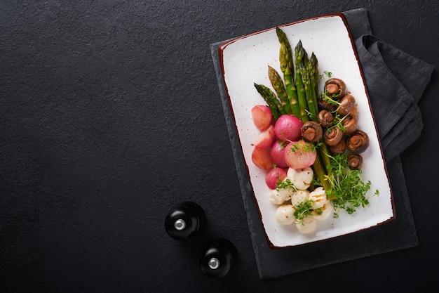 Asparagus mushrooms mozzarella cheese grilled radish and cress salad oil olive salad on rectangular ceramic plate on black concrete table background Healthy diet grilled food concept Top view