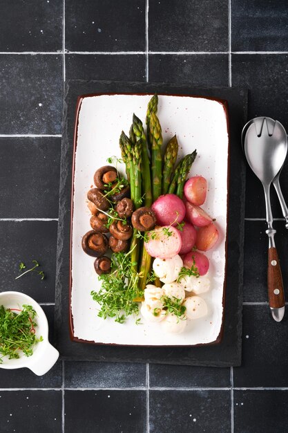 Asparagus mushrooms mozzarella cheese grilled radish and cress salad oil olive salad on rectangular ceramic plate on black old tile table background Healthy diet grilled food concept Top view