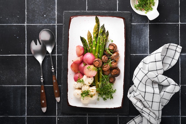 Asparagus mushrooms mozzarella cheese grilled radish and cress salad oil olive salad on rectangular ceramic plate on black old tile table background Healthy diet grilled food concept Top view