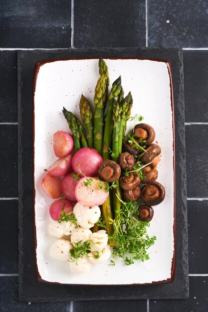 Asparagus mushrooms mozzarella cheese grilled radish and cress
salad oil olive salad on rectangular ceramic plate on black old
tile table background healthy diet grilled food concept top
view