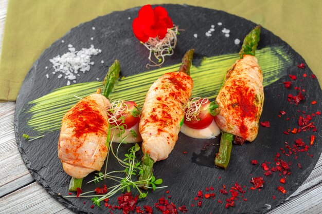 Asparagus rolled with chicken meat slices served on dark plate