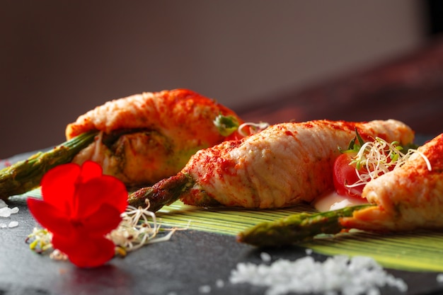 Asparagus rolled with chicken meat slices served on dark plate