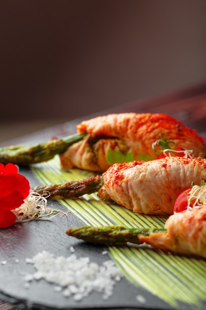 Asparagus rolled with chicken meat slices served on dark plate