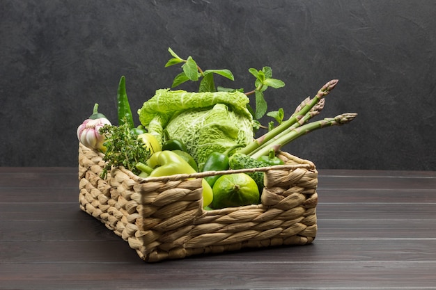 Asparagus, Savoy cabbage, lime and pepper in rattan basket. Dark Wooden background. Copy space