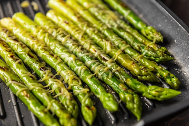 Photo asparagus sprinkled with parmesan cheese fried in a pan
