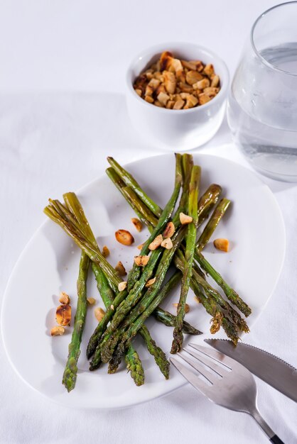 Asperges geroosterd in olijfolie met gemalen walnoten en saus op een witte plaat. Vegetarisch eten.