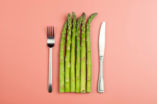 Asperges met mes en vork op een roze ondergrond