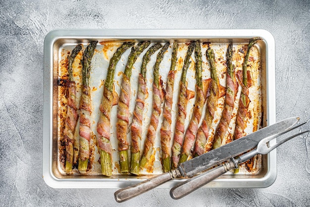 Asperges verpakt in spek op een barbecue dienblad. Witte achtergrond. Bovenaanzicht.