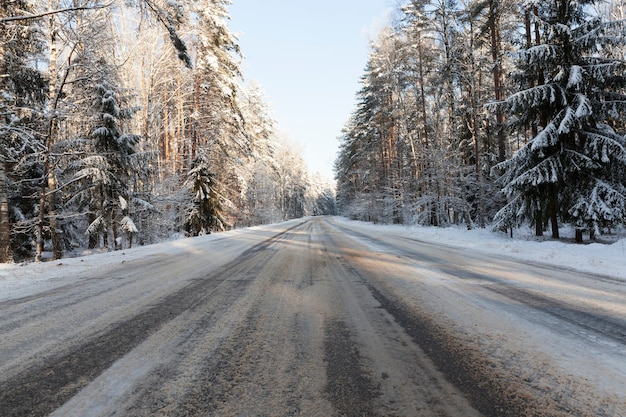 降雪後の雪が降った道路のアスファルト部分、フレーム中央の空、雪の吹きだまりと雪に覆われた森の中を道路が建設されています