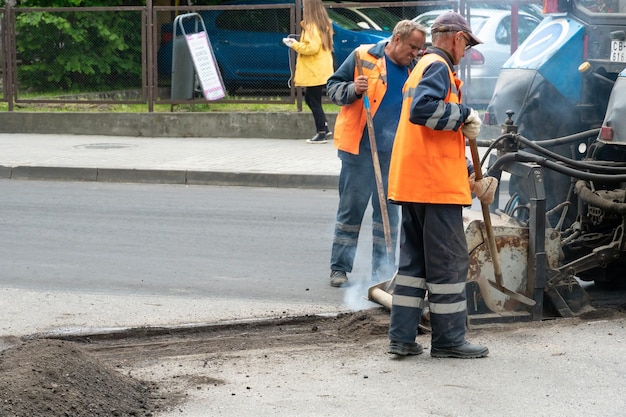 Foto riparazione dell'asfalto in città una squadra di operai in abiti speciali si trova accanto a un trattore e a un'attrezzatura per la posa dell'asfaltato