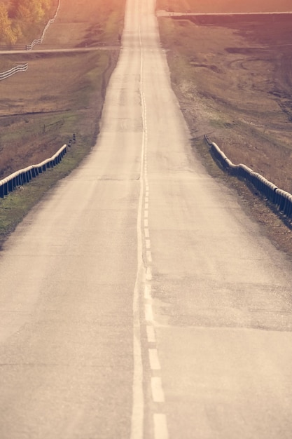 Asphalt road stretches into the distance among the beautiful nature at sunset Toned