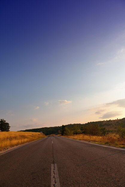 Asphalt road through the green field and clouds on blue sky in summer day