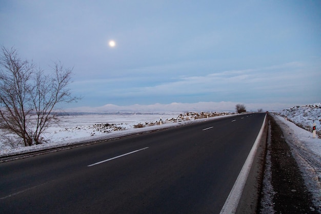 Strada asfaltata con paesaggio innevato la sera