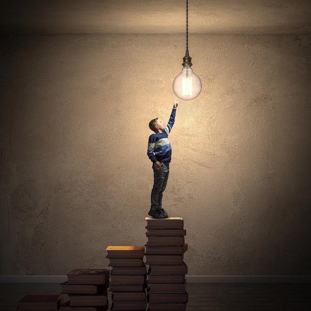 Foto aspirant jonge geest reiken naar gloeilamp op boeken