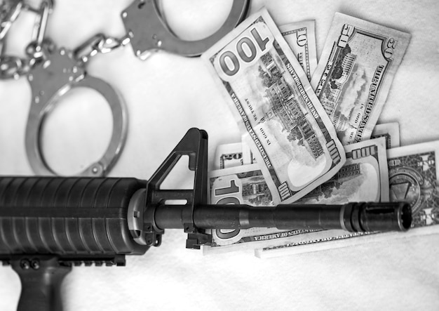 Assault black rifle muzzle. black and white of modern automatic\
high powered rifles and police handcuffs on dollar currency. copy\
space. financial, crime, mafia, terrorism banner, armed conflict.\
usa