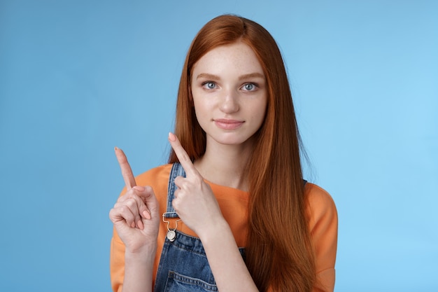 Assertive goodlooking redhead girl know what talking about pointing upper left corner index fingers showing confidently good product recommend check out standing blue background