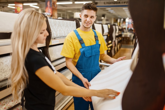 Assistant and female customer choosing wallpapers in hardware store. Seller in uniform and woman in diy shop, shopping in building supermarket