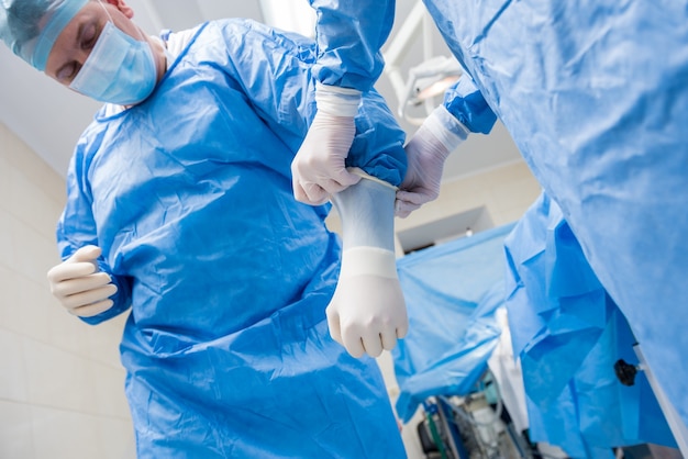 L'assistente aiuta il chirurgo a indossare guanti in lattice e camice chirurgico prima dell'operazione