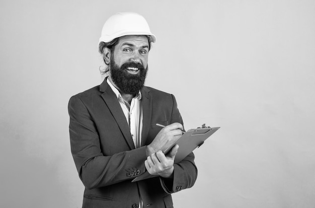 Assistant male builder wearing formal suit and helmet for protection working on construction project happy man with beard wear hard hat concept of engineering architecture and building