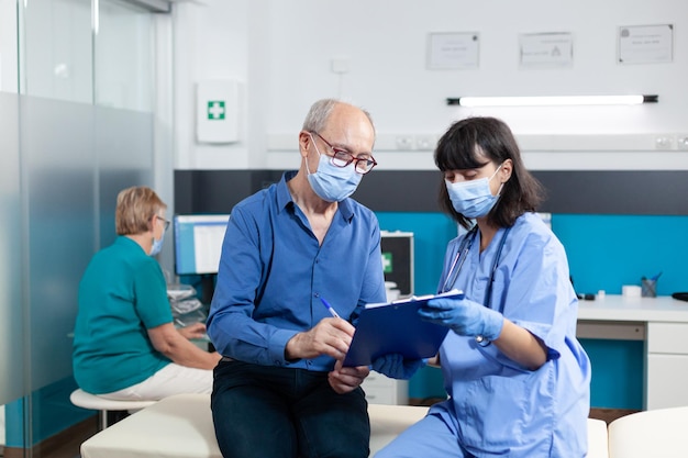 Assistente che parla con un pensionato con maschere per il controllo. donna che lavora come infermiera facendo consulenza medica per osteopatia e assistenza sanitaria con uomo anziano durante la pandemia di coronavirus