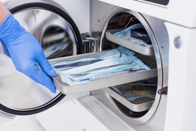 Assistants hand in gloves insert packaged dental instrument to the autoclave to sterilise