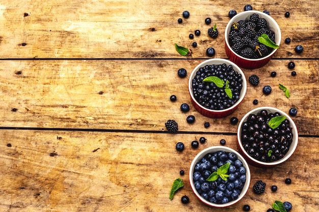 Assorted berries in blue and black colors: bilberry, blueberry, currant and blackberry. Old wooden table background, top view